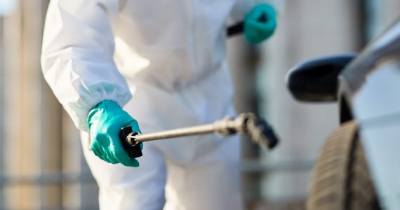 Close-up of man in protective suit disinfecting car tire during coronavirus epidemic.