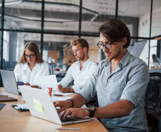 Guy in glasses in front of his employees. Young business people in formal clothes working in the office.